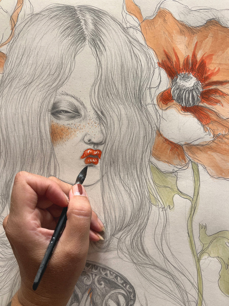 Main de Miss Van peignant un dessin à l’aquarelle, détail du visage féminin avec fleur et lèvres rouges.