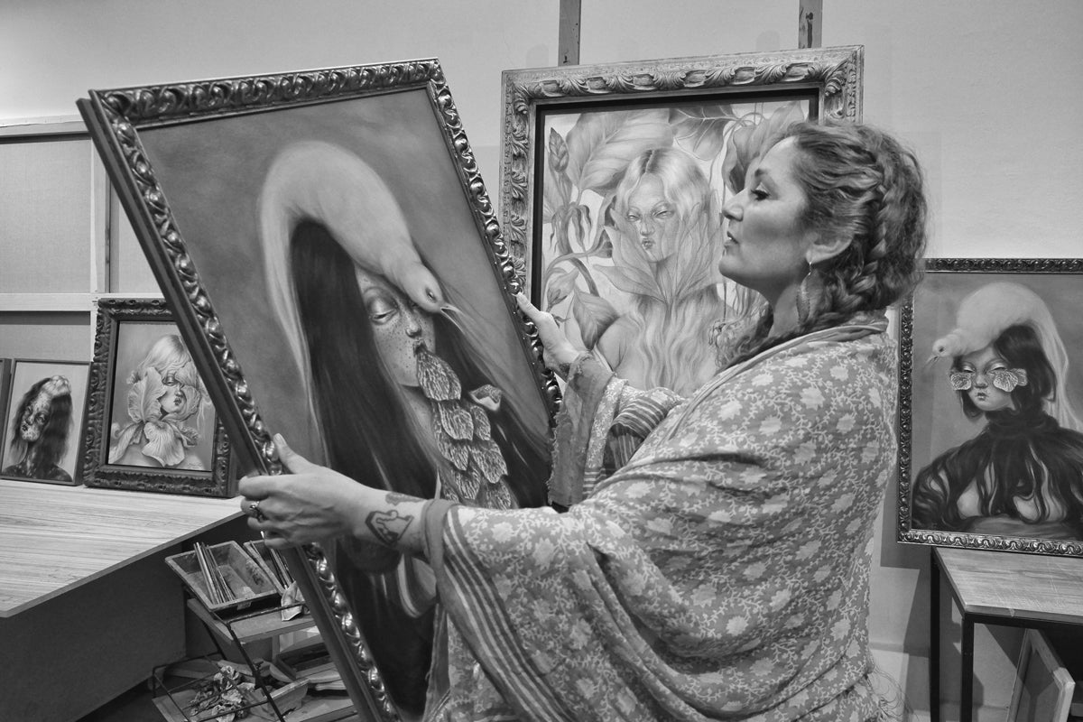 Portrait de Miss Van dans son atelier, entourée de ses peintures figuratives encadrées.