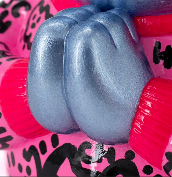 Gros plan sur les mains bleu métallisé d’une sculpture signée CHANOIR, capturant les détails texturés de la résine peinte à la main. L’œuvre, aux teintes vibrantes de rose et de graffiti noirs, est une épreuve d’artiste, soulignant l’authenticité et la finesse du travail artisanal. Style street art, pop, Figuration Libre, fusionnant urban art et sculpture contemporaine.