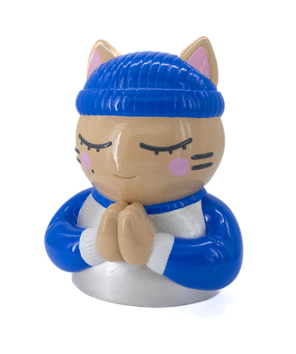 Vue trois-quarts droit de la sculpture "Foi" par CHANOIR – œuvre collector originale. Chat beige aux yeux clos, coiffé d’un bonnet bleu roi et vêtu d’un maillot blanc nacré avec manches bleu roi et aux bordures blanches. Pièce originale peinte à la main, fusion de street art et art contemporain.