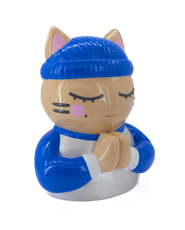 Vue trois-quarts droit de la sculpture "Foi" par CHANOIR – œuvre originale. Chat beige aux yeux clos, coiffé d’un bonnet bleu vif et vêtu d’un maillot blanc nacré avec manches bleu vif et bordures blanches. Pièce unique peinte à la main, fusion de street art et sculpture contemporaine.
