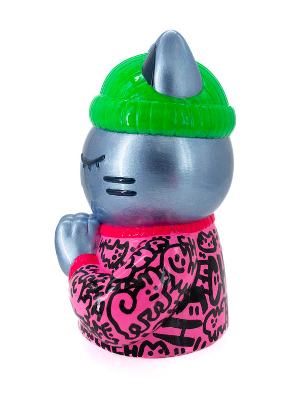 Vue de profil de l'épreuve d'artiste de la sculpture, signée CHANOIR. Cette oeuvre unique est un félin coiffé d'un bonnet vert fluo et d'un sweat rose à graffitis noirs. Une sculpture colorée et pop.