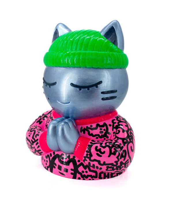 Vue trois-quarts gauche de l’épreuve d’artiste CHANOIR – Sculpture unique peinte à la main. Chat argenté aux yeux clos, coiffé d’un bonnet vert vif et vêtu d’un t-shirt rose à motifs graffiti noirs. Pièce exclusive fusionnant street-art et sculpture contemporaine.